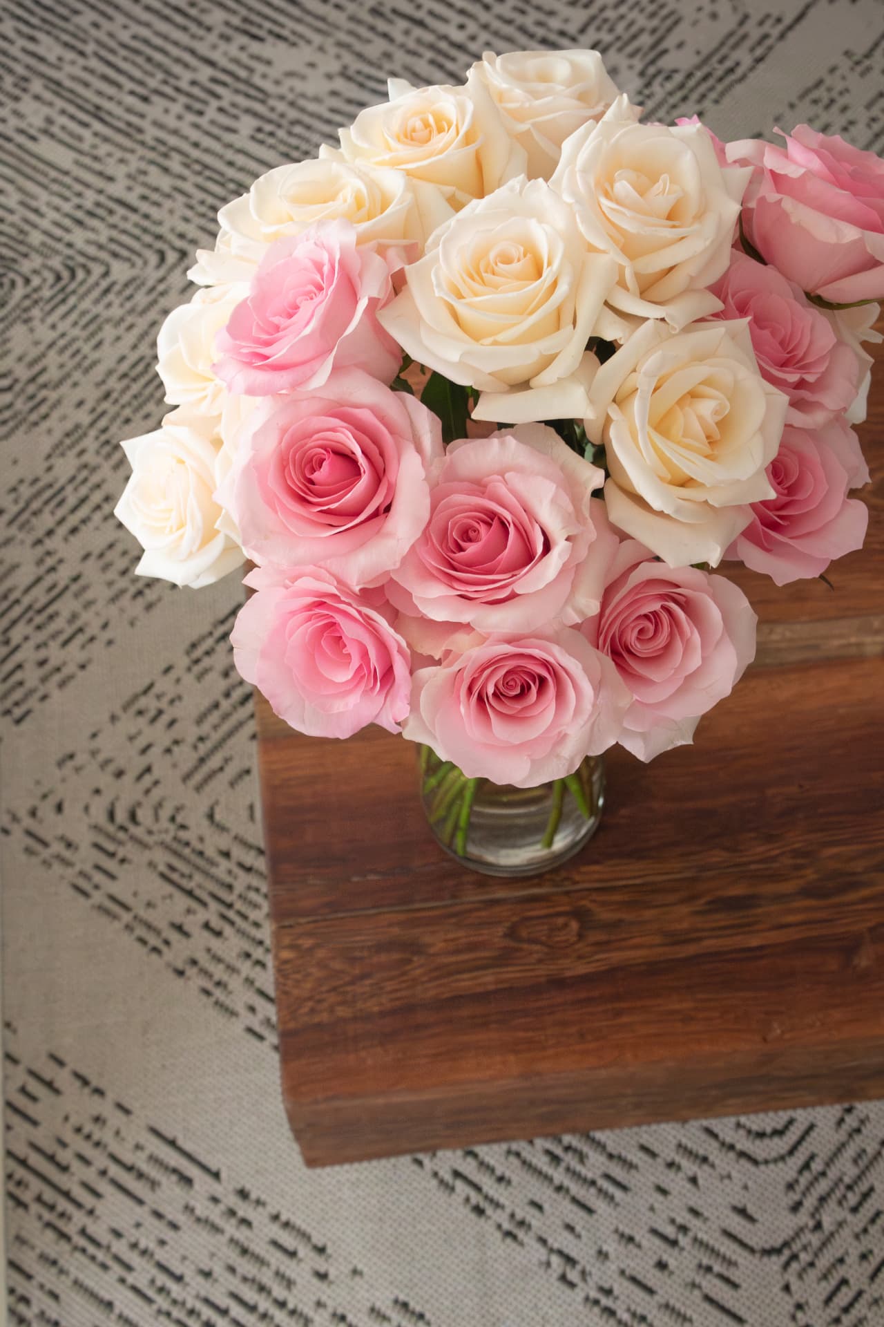 Cream and pink roses arranged in a glass vase on a wood table
